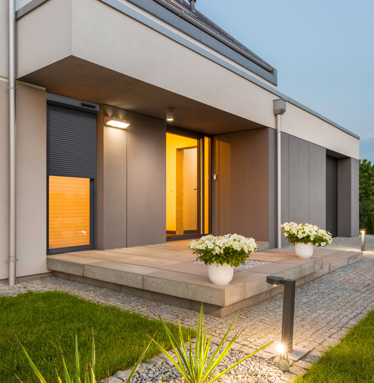 Vue extérieur d'une maison moderne beige et noir, avec une terrasse avec des pots de fleurs. Des volets roulants Renosun anthracite de la marque Flip aux fenêtres