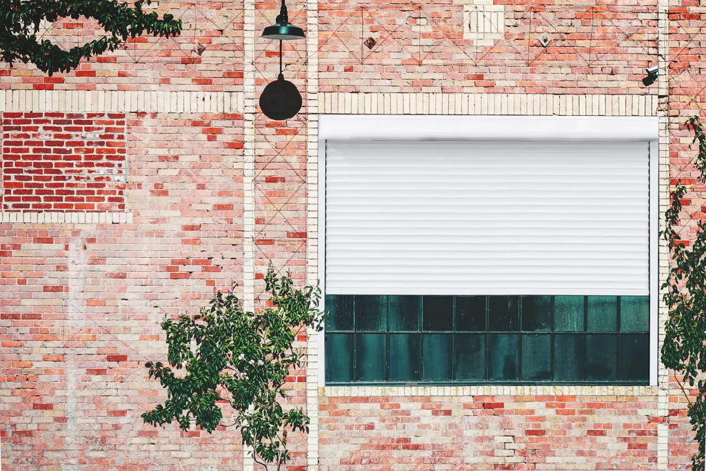 Façade d'une maison en brique style industriel avec du lierre et une lampe, volet roulant renosun blanc de la marque Flip