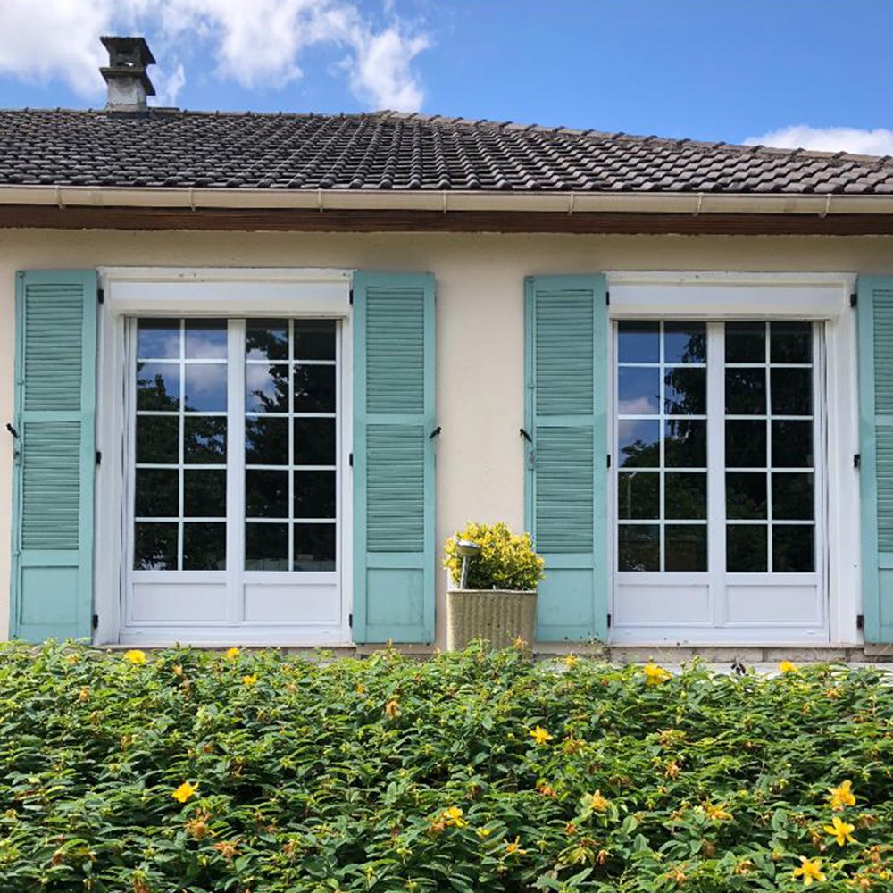 Façade d'une maison avec des volets en bois vert d'eau et des volets roulants renolux astrolux blancs de la marque Flip