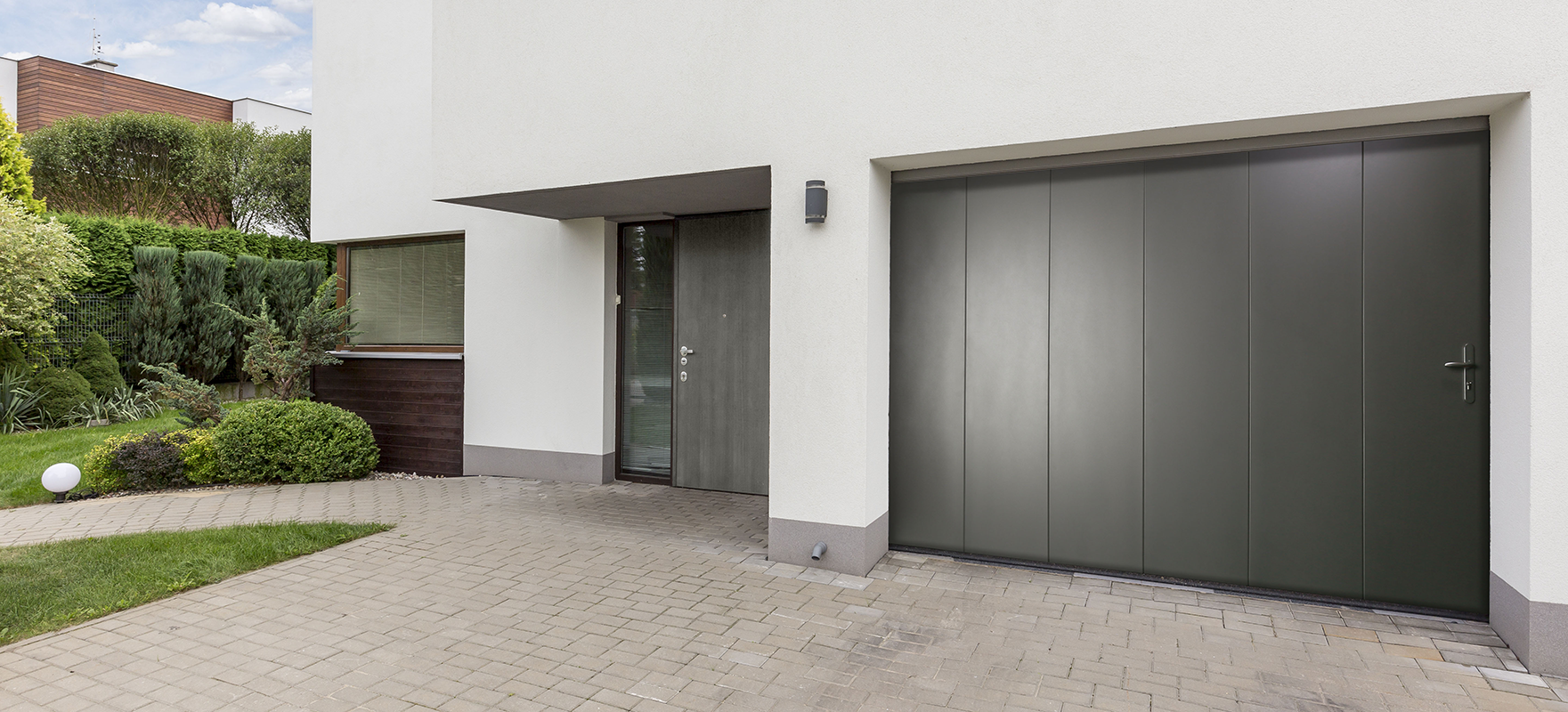 Maison moderne blanche avec une porte de garage sectionnelle latérale noire et un portillon de la marque Flip