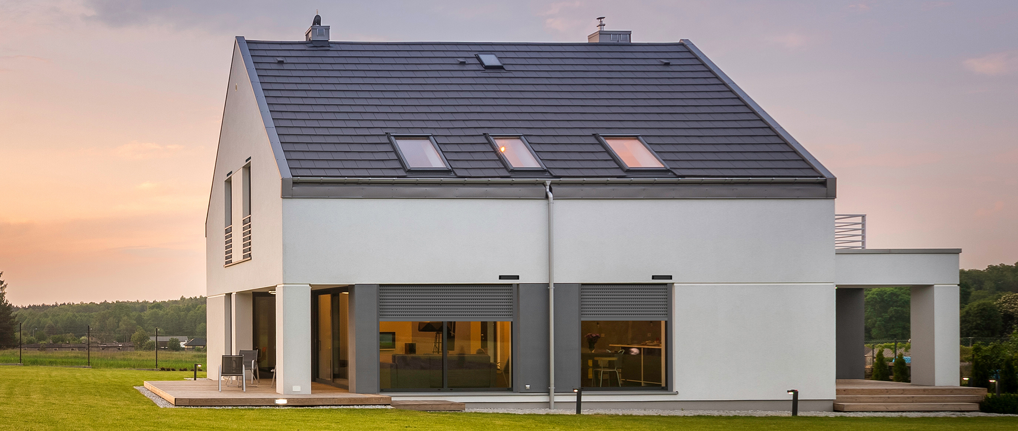 Vue extérieure d'une maison, devant un couché de soleil, équipée de volets roulantrs Bloc in Sun de la marque Flip