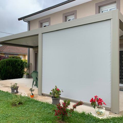 Terrasse d'une maison entourée d'un store zip soltis perform 92 gris monté sur une pergola