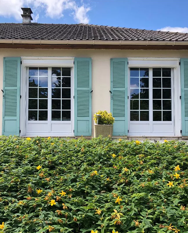 Façade d'une maison avec des volets en bois vert d'eau et des volets roulants renolux astrolux blancs de la marque Flip