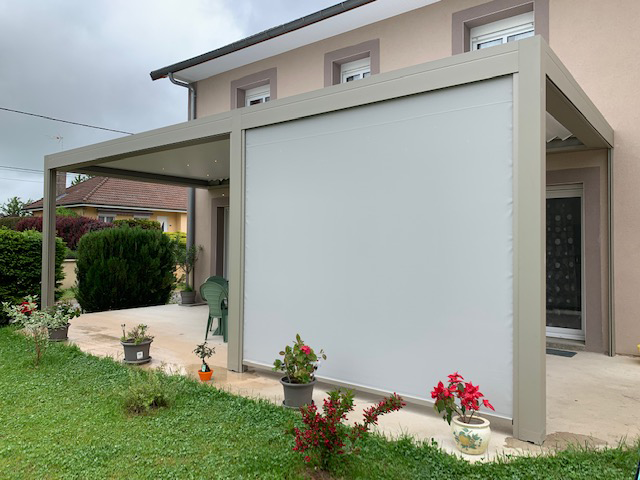 Terrasse d'une maison entourée d'un store zip soltis perform 92 gris monté sur une pergola